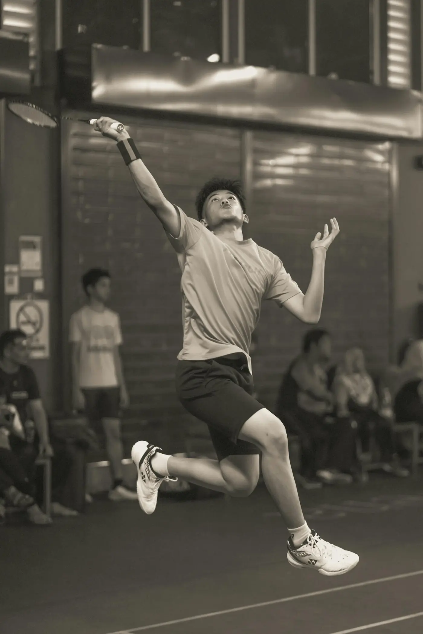 A badminton player leaping into a jump smash on an indoor court